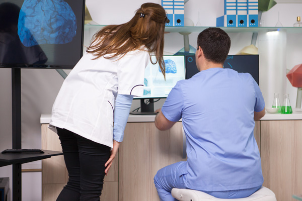male and female pathologists in scrubs working at a computer